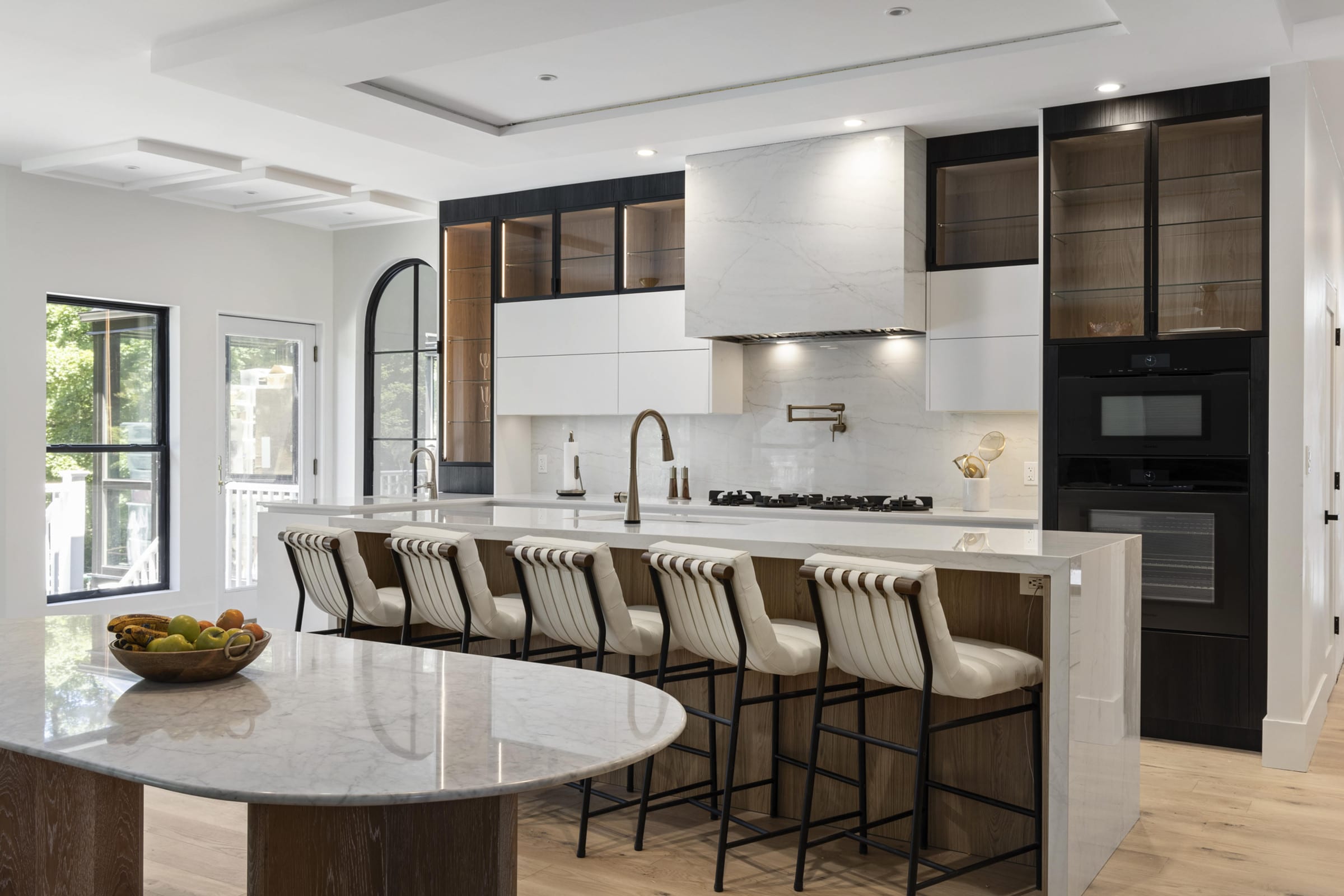 White and walnut kitchen with black glass cabinets and a curved marble island, North Haven CT
