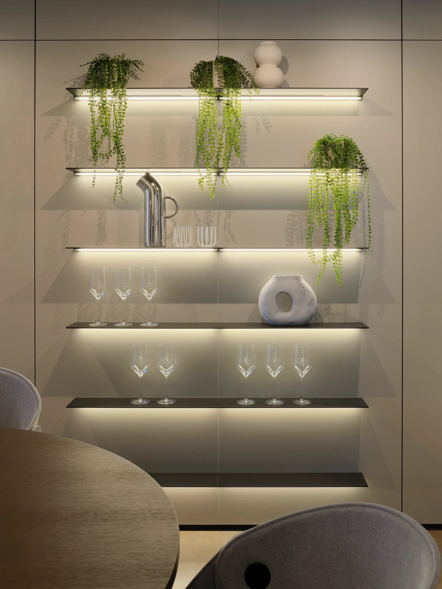 Wall of lit floating glass shelves beside a dining table